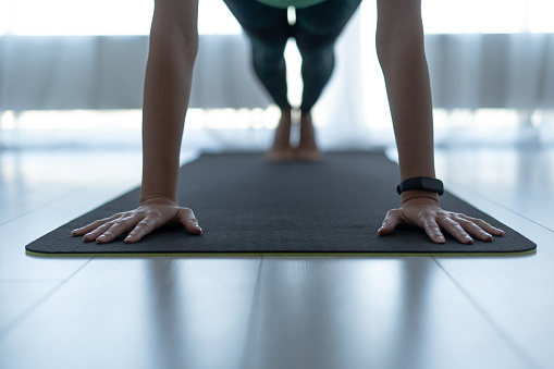 Ausgeschnittene Ansicht einer sportlichen und jungen erwachsenen Frau, die zu Hause Power Yoga praktiziert und eine Plankenpose auf einer Fitnessmatte macht