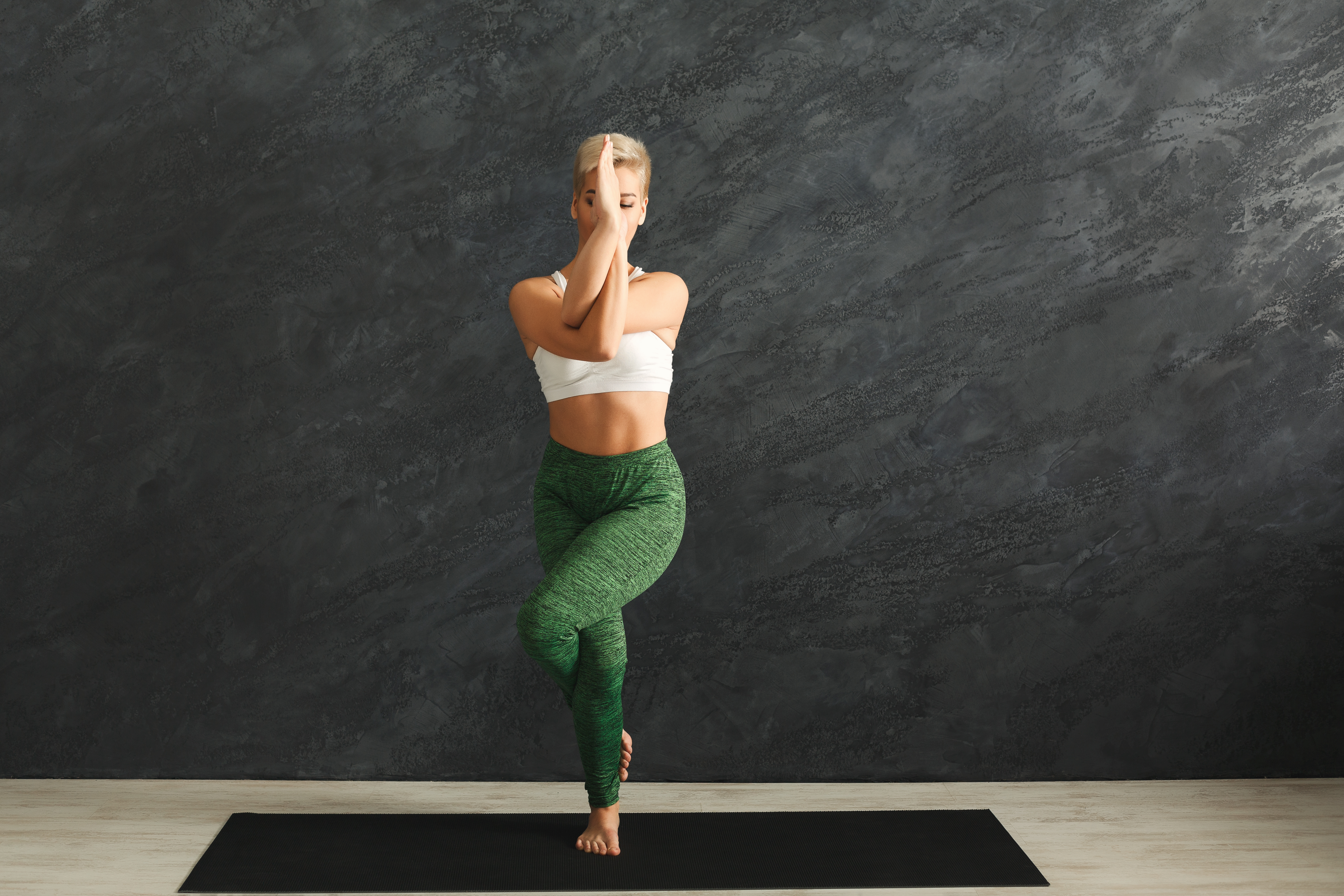 Fitness, Frau trainiert Power Yoga in Adlerpose im Fitnessstudio vor grauem Hintergrund, Kopierraum. Junges schlankes Mädchen macht Sport.
